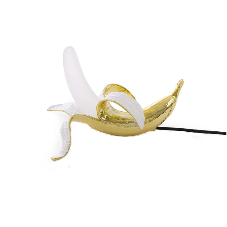 Banana table lamp with gold banana body, white bulb, and black power cord