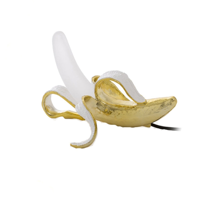 Banana-shaped table lamp with gold banana body and white bulb, curled pose
