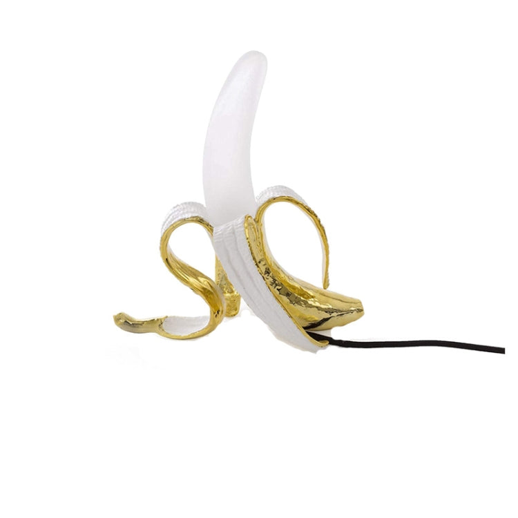 Banana-shaped table lamp with white peel and gold finish, upright with black power cord