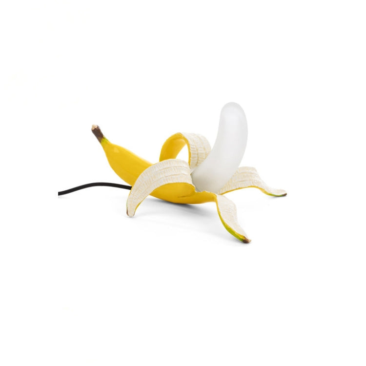 Banana-shaped table lamp with yellow banana and white peel, lying down with black cord