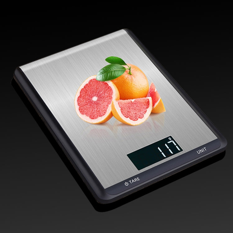 Stainless steel kitchen digital scale with fruit on top and green-lit digital display
