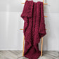 Thick knitted wool blanket, wine red, draped over a stand with textured knit