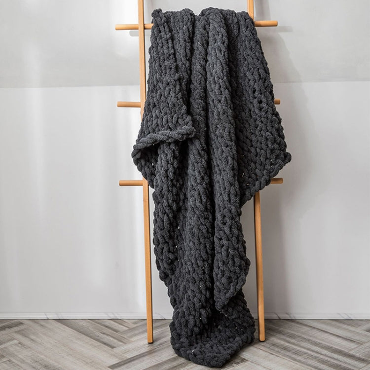 Dark gray chunky cable-knit wool blanket with thick textured weave, draped on a stand