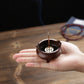 Small copper incense burner held in hand, with central stick and perforated insert