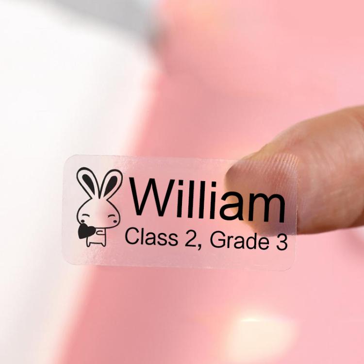 Transparent label sticker with printed name and bunny icon, held by fingertip
