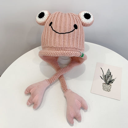 Pink knitted frog hat for toddlers with smile face, big white eyes, and long tie flaps
