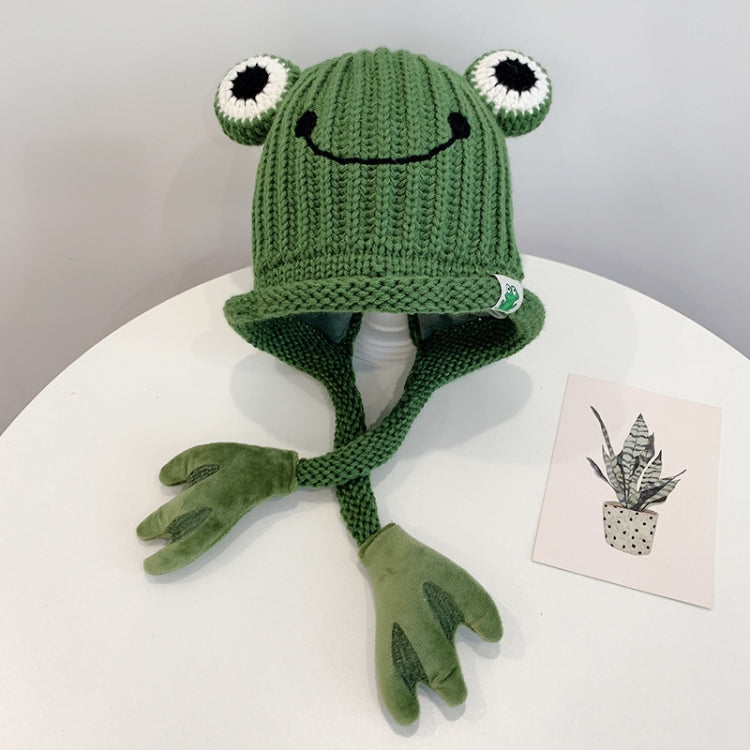 Green knitted frog hat for toddlers with smile face, big white eyes, and long tie flaps