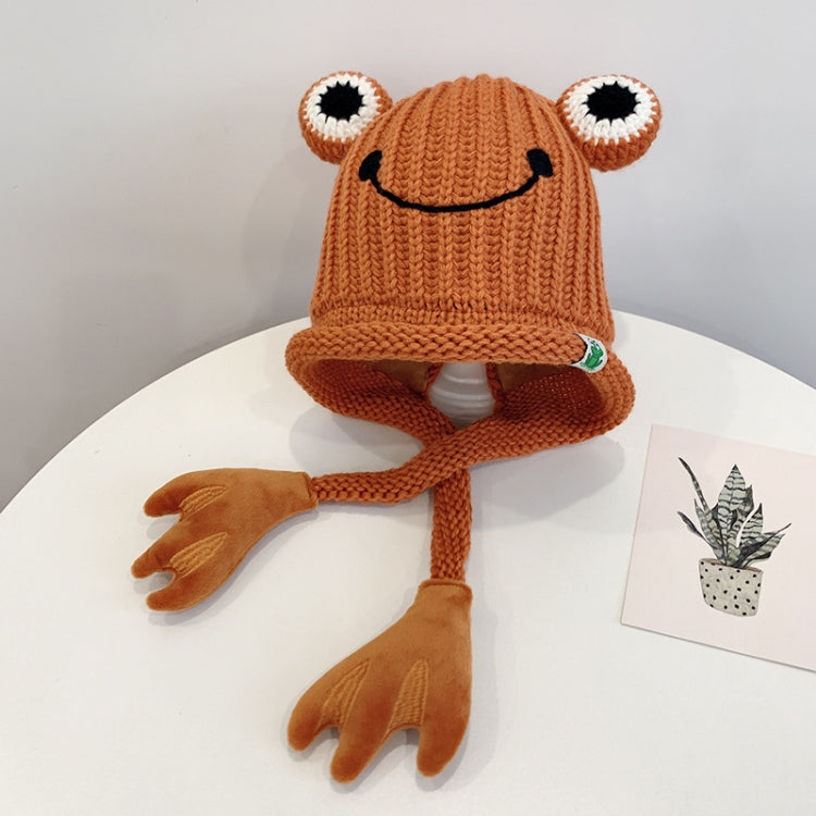 Orange knitted frog hat for toddlers with smile face, big white eyes, and long tie flaps