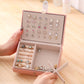 Pink jewelry storage box open with compartments showing many stud earrings and rings