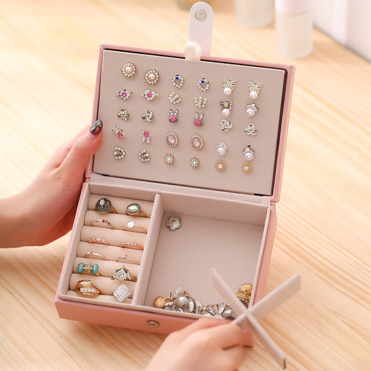 Pink jewelry storage box open with compartments showing many stud earrings and rings