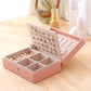 Pink jewelry storage box open with divided compartments and display panel of stud earrings