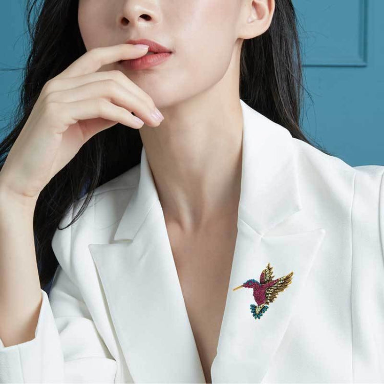Small blue and gold rhinestone bird brooch on a white blazer lapel
