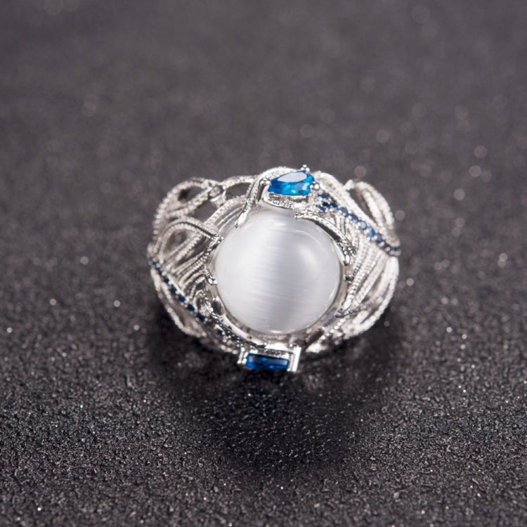 Silver-tone ring featuring oval white stone with blue side gems and ornate feather work