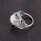 Silver-tone openwork ring with oval white stone and blue center gem, feather pattern