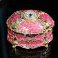 Gold-trim pink oval jewelry storage box with diamond-style center top and raised side filigree