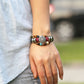 Beaded leather bracelet worn on wrist with circular charm, blue and red beads, metal tubes