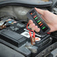 Hand holding a battery tester with clip leads on a car battery