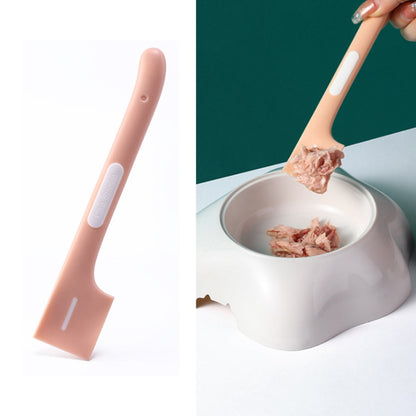Pink long-handled cat-shaped spoon mixing wet pet food in a metal bowl.