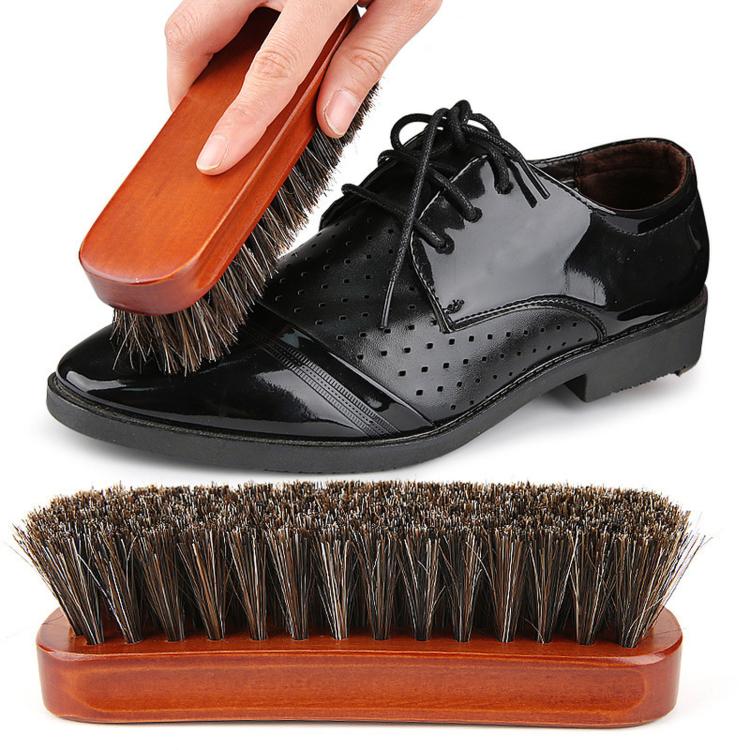 Wood shoe dust brush with dark bristles being used on a black lace-up shoe