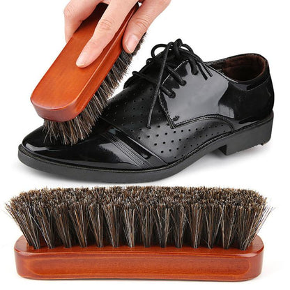 Wood shoe dust brush with dark bristles being used on a black lace-up shoe