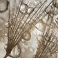 Close-up of abstract metallic droplets and branching lines in warm gray and gold tones