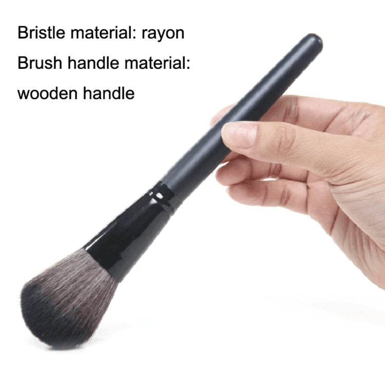 Powder makeup brush with soft dark bristles on a black handle, held in a hand