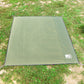 Green waterproof outdoor mat with logo patch and corner stakes on grass