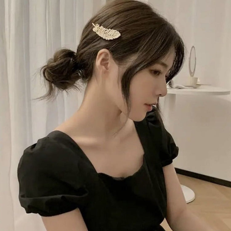 Gold-tone leaf hair clip worn in dark hair, small decorative barrette