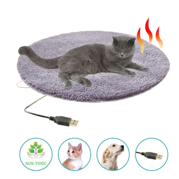 Gray cat resting on round purple plush pet heating pad with USB cable