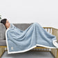 Misty blue flannel shawl blanket with white fleece trim laid over couch armrest