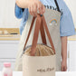 Round insulated lunch bag lifted by brown handles, beige exterior with drawstring