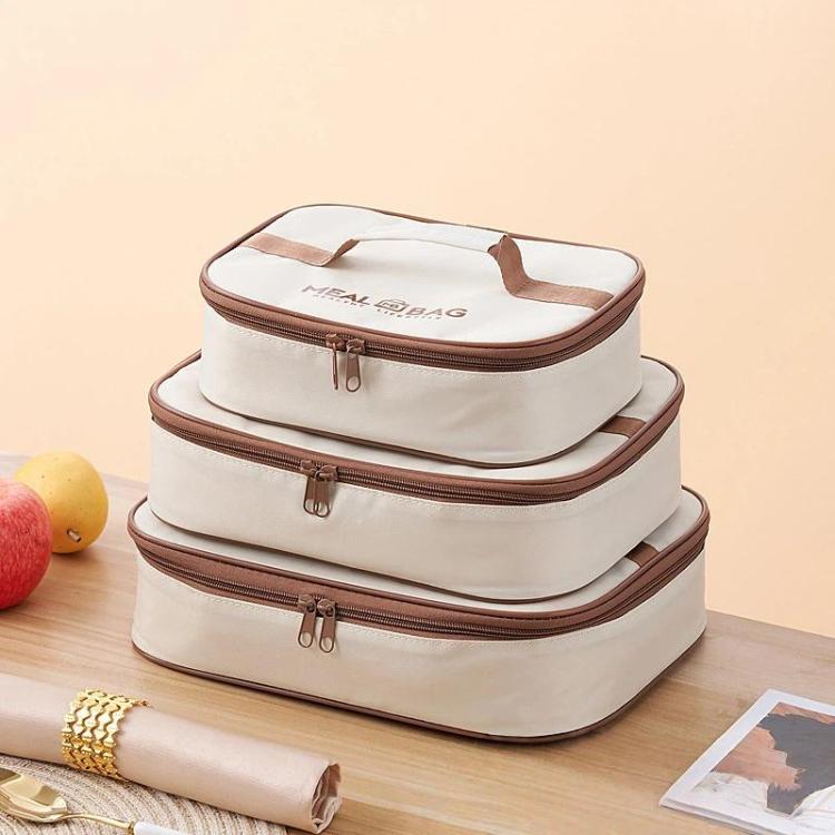 Stacked cream insulated lunch bags with brown zippers and handles, set shown
