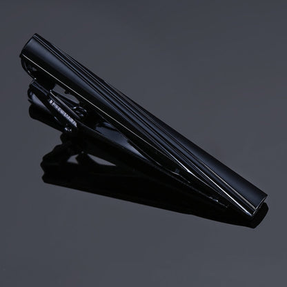 Black glossy tie clip with slim ridged bar and hinged clasp, polished metal finish.