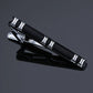 Black and silver striped tie clip with engraved line accents and hinged clasp.