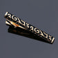 Black tie clip with gold swirl pattern and gold-tone borders, glossy finish, clasp visible.