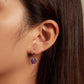 Heart-shaped purple zirconia illusion drop earrings on ear with hinged hoops