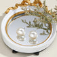 White pearl stud earrings with domed round fronts, shown in a decorative tray