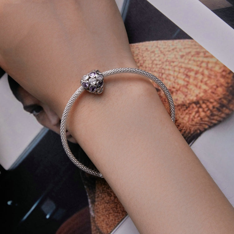Silver mesh bracelet on wrist with heart-shaped zirconia bead in purple and clear