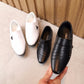 Black and white kids leather-look dress shoes, held by a hand, strap closure