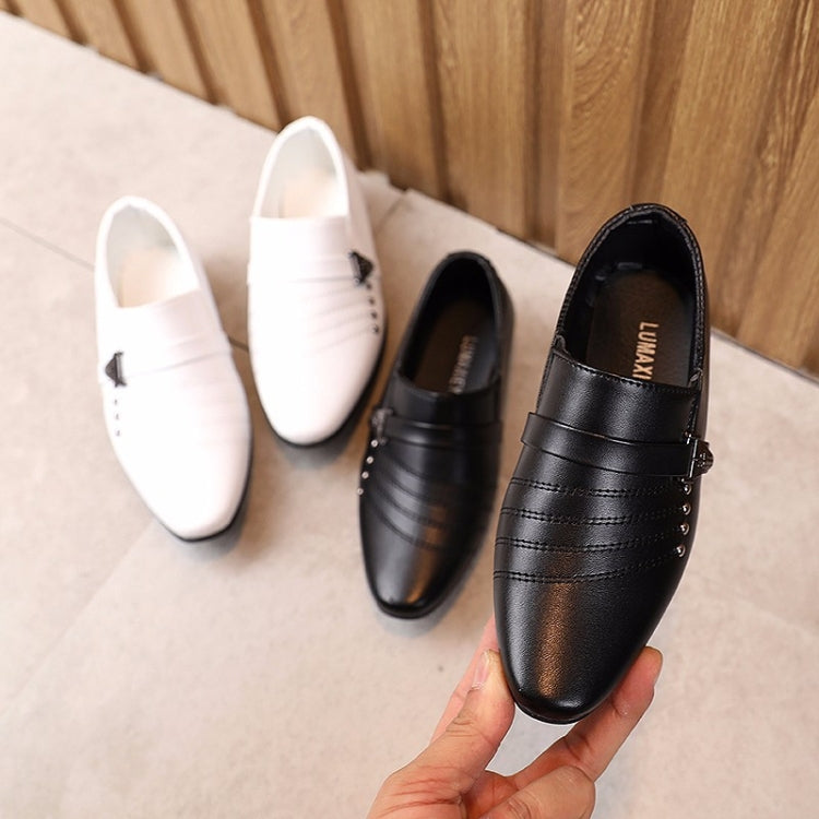 Black and white kids leather-look dress shoes, held by a hand, strap closure