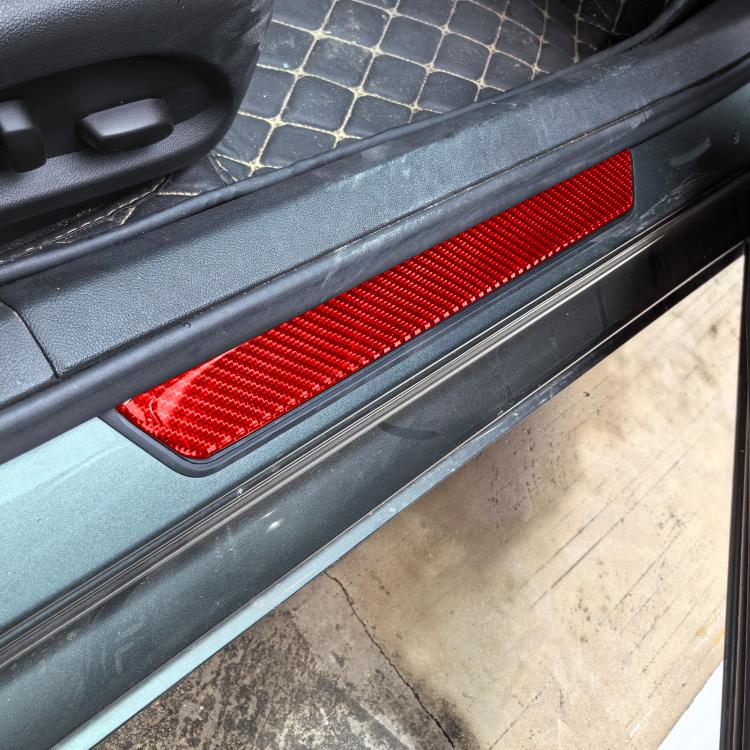 Red carbon-fiber door sill sticker installed on car threshold, close-up view