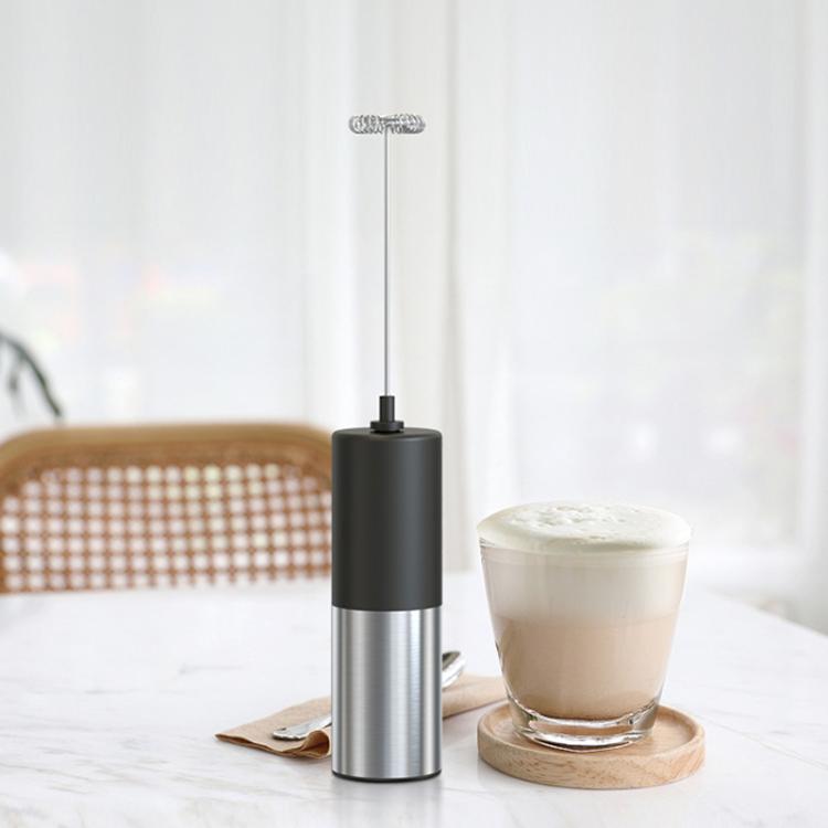 Handheld milk frother standing next to a glass cup of foamy milk.