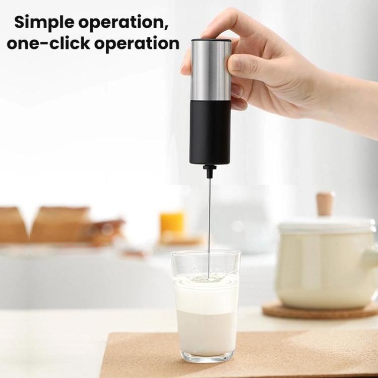 Handheld milk frother held above a glass cup to froth milk.