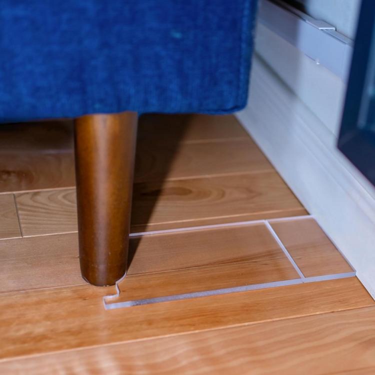 Acrylic sofa leg floor gasket with curved base, placed on wooden floor tiles