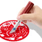 Hand using metal engraving cutter on red decorative paper disc