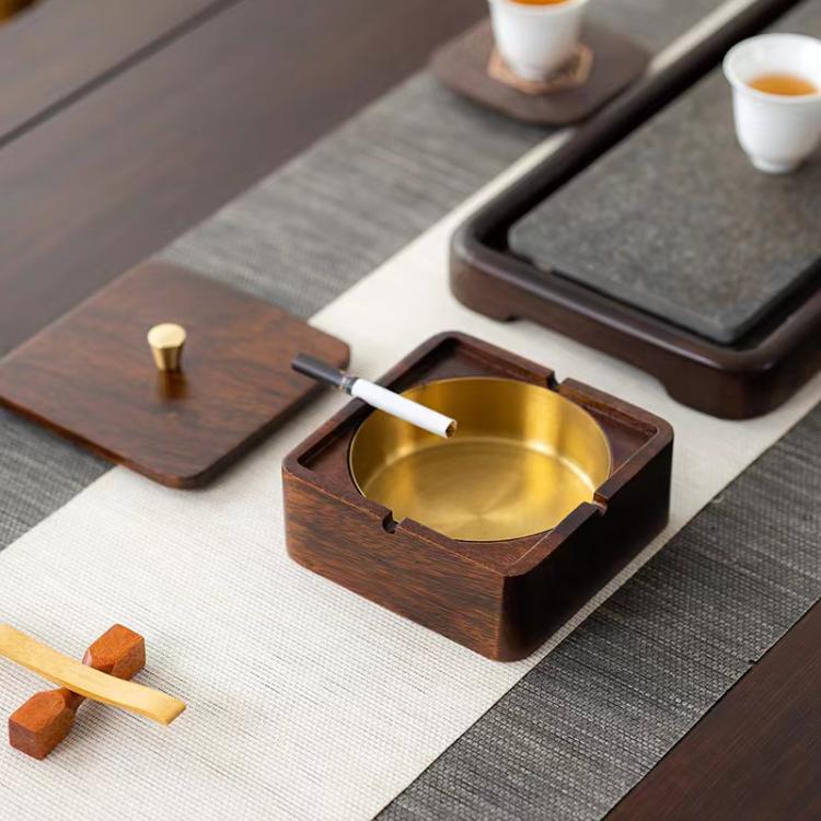 Square walnut wood ashtray with brass bowl, lid open, cigarette held near tray