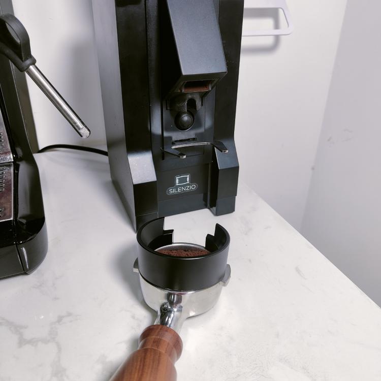 Black magnetic dosing ring cup attached under grinder, holding a scoop of grounds.