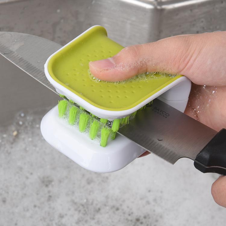 Knife cleaning brush held against a metal knife blade with suds