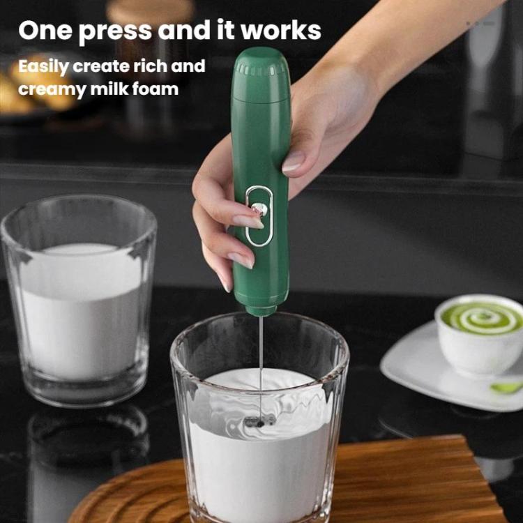 Green handheld milk frother whisk blending milk foam in a clear glass