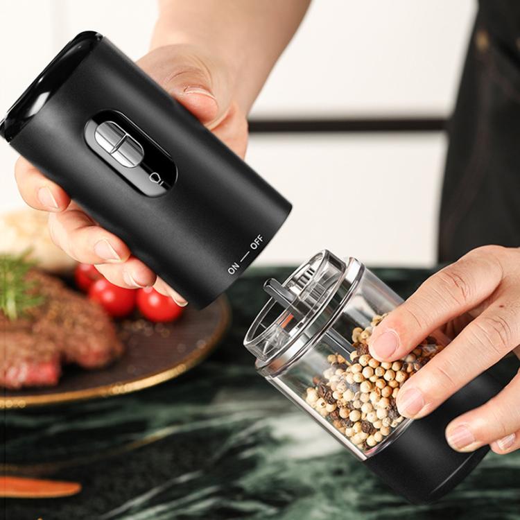 Black electric grinder in hand with empty glass insert being filled with peppercorns